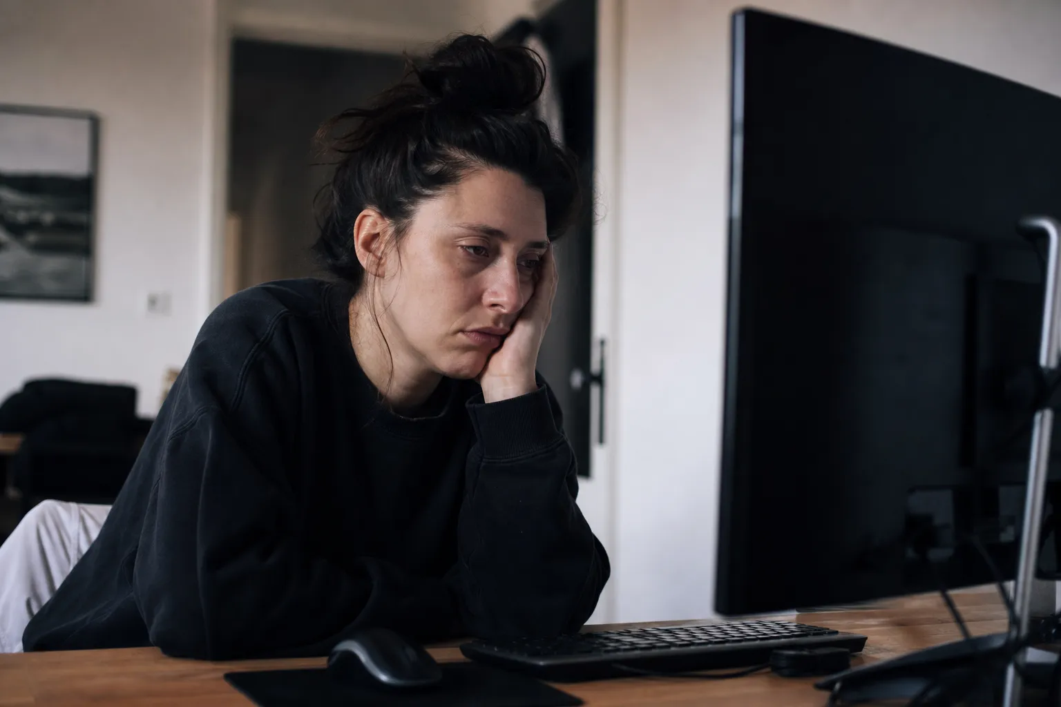 image of a person frustrated and tired of the job search process. They are sitting defeated in front of a powered off screen. You can definitely tell it's off as they stare dead-eyed into it as if they have spent every bit of energy applying today.